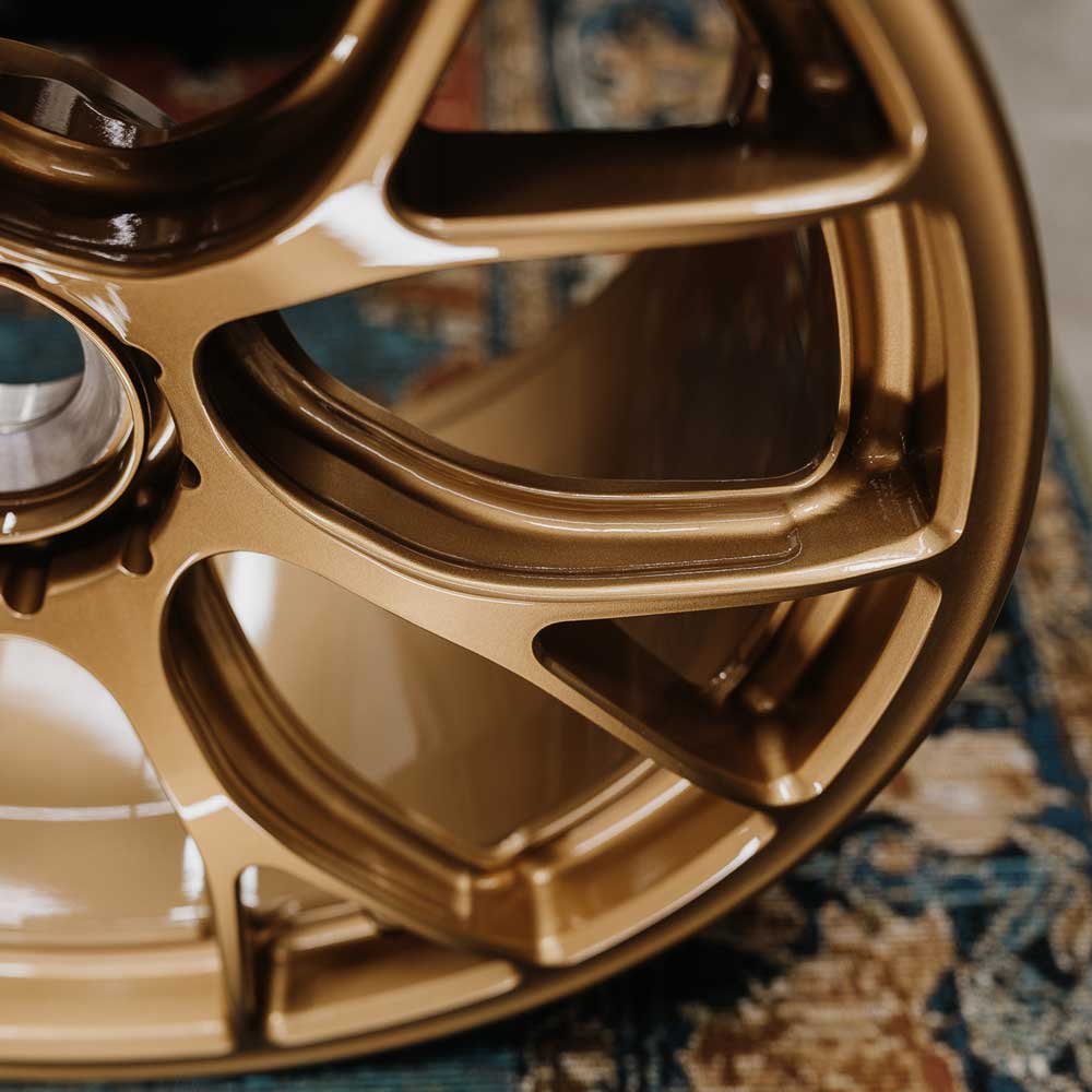 High-performance forged alloy wheel in bronze finish showcasing deep concave spokes and big brake caliper clearance (X-Factor).